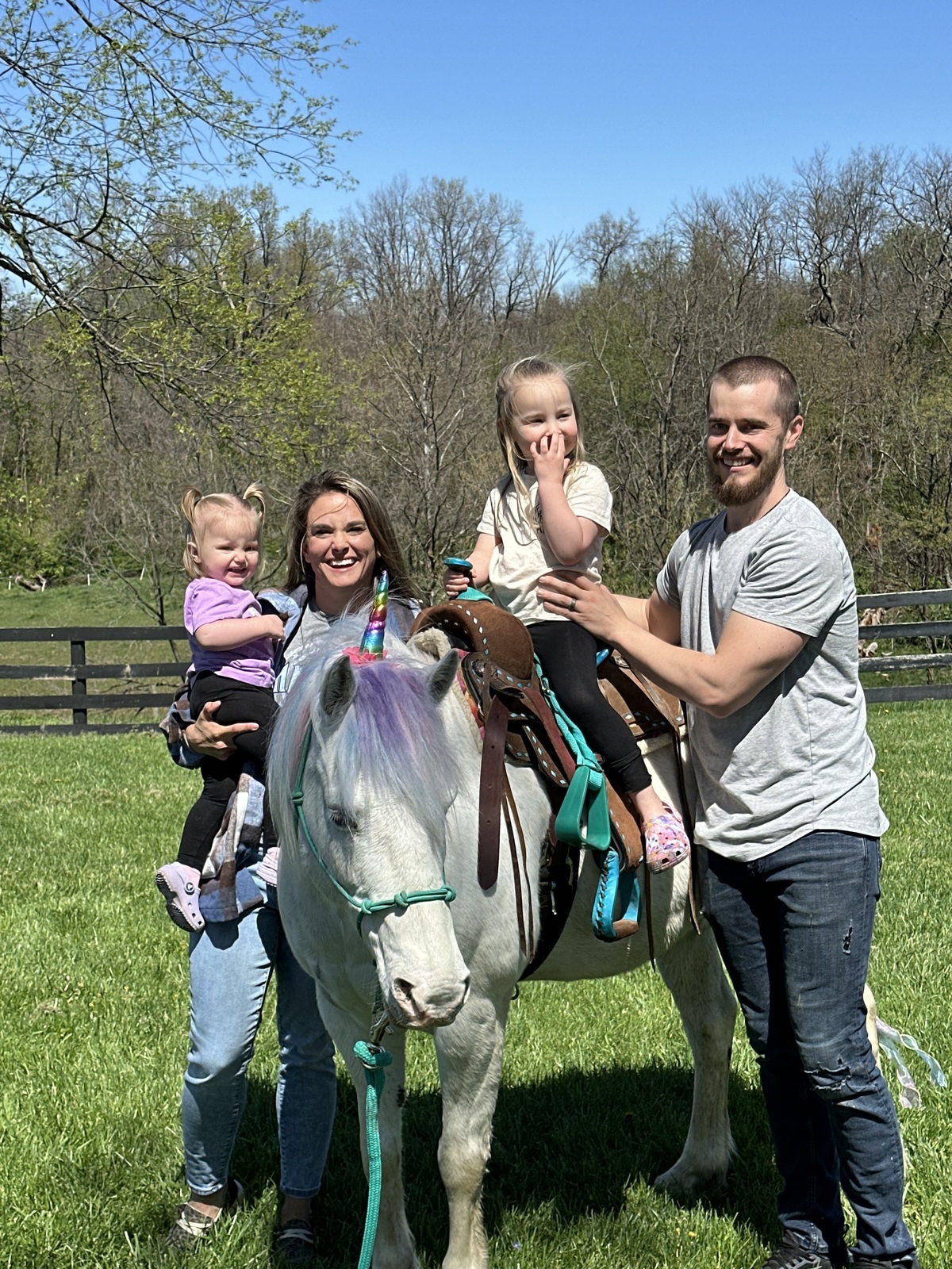 A smiling family consisting of a man, a woman, and two young girls, one of whom is on a horse